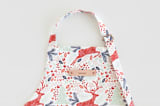 "Jumping Reindeer" - Personalizable Children's Apron in Red by Phrosné Barwood - Tag in Bodoni Regular