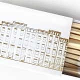 "Cozy Village Matchbox, Gold on White" - Matchbooks and Matches in gold by Jessica Cunningham
