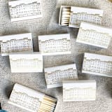"Cozy Village Matchbox, Gold on White" - Matchbooks and Matches in gold by Jessica Cunningham