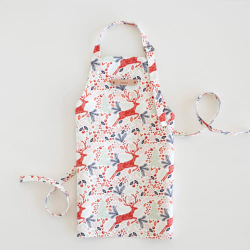 This is a red kids aprons by Phrosné Barwood called jumping reindeer in standard