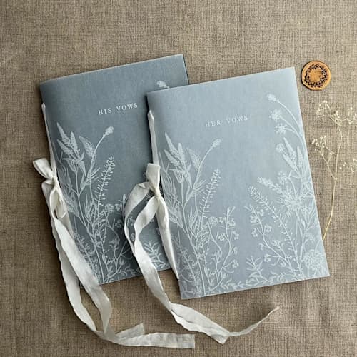 This is a blue vow books by Ivory Invitations called white ink print vellum covered english botanical garden blue vow books | set of 2 books | includes 1 her vows and 1 his vows in standard