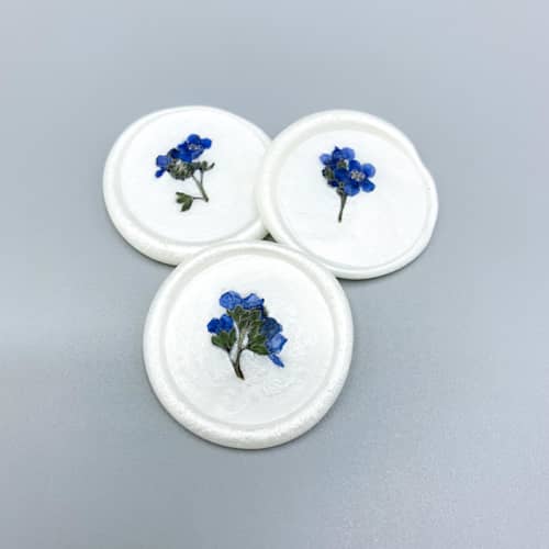 This is a blue wax seals by Christine OMalley called pressed flower ivory wax seal blue forget me not set of 6 in standard