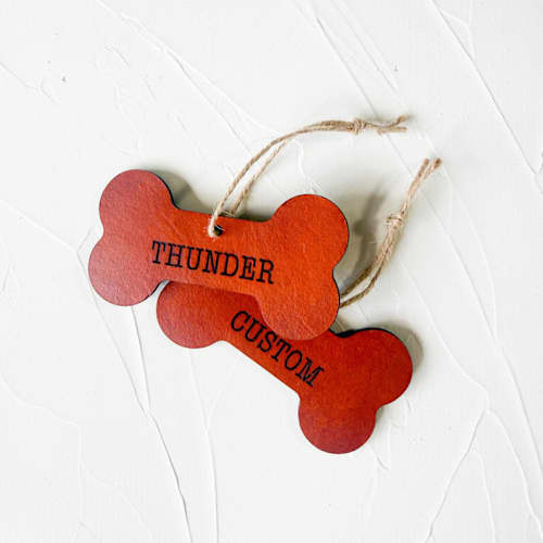 This is a brown holiday decorations by Left Grain called personalized leather dog bone ornament in standard