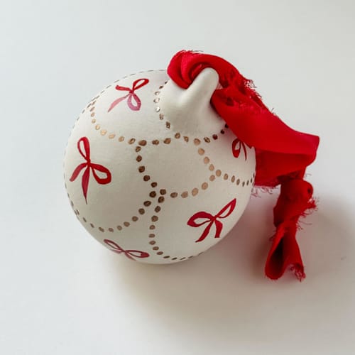 This is a red holiday decorations by Kara Aina called bronze & red mini bow hand painted ceramic ornament in standard