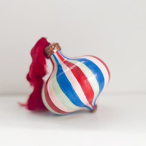 This is a multicolor holiday decorations by Mary Gaspar called red, pink and blue striped ornament with red ribbon in standard