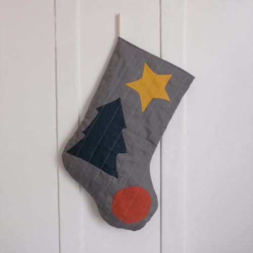 This is a gray holiday decorations by Quiet Goods called charcoal quilted stocking with multi-color appliqué details no.1 in standard