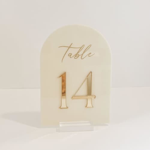 This is a gold table numbers by Alexandra Ettis called ivory & gold arch acrylic table number in standard